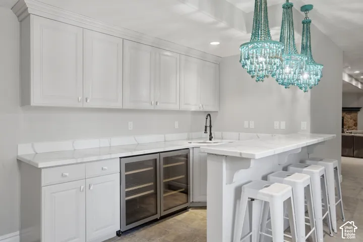 Custom white cabinetry with crown molding, stone-surface countertops, built-in dual wine refrigeration units, matte black gooseneck faucet, and decorative beaded chandelier lighting