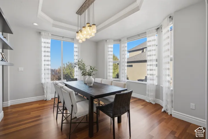 Tray ceiling featuring a multi-light pendant fixture, wood-finish flooring, bay window configuration, and built-in wall shelving