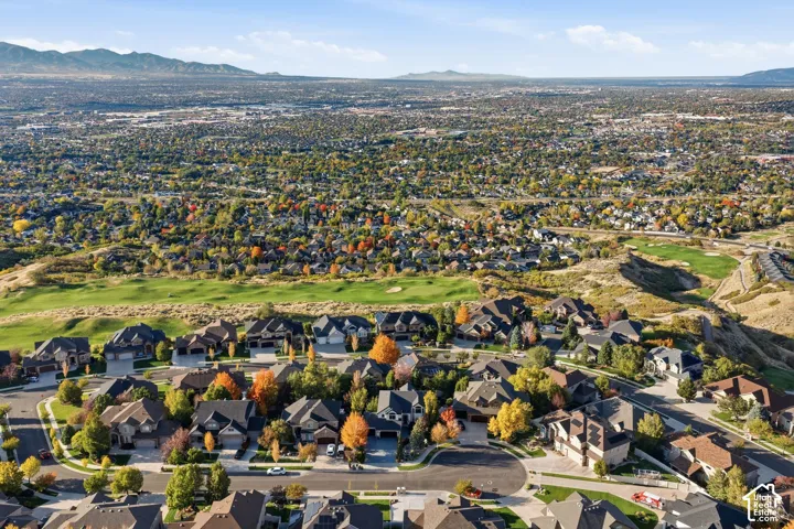 Aerial perspective of a hillside residential community featuring multi-level homes, asphalt-paved streets, established trees, and mountainous terrain
