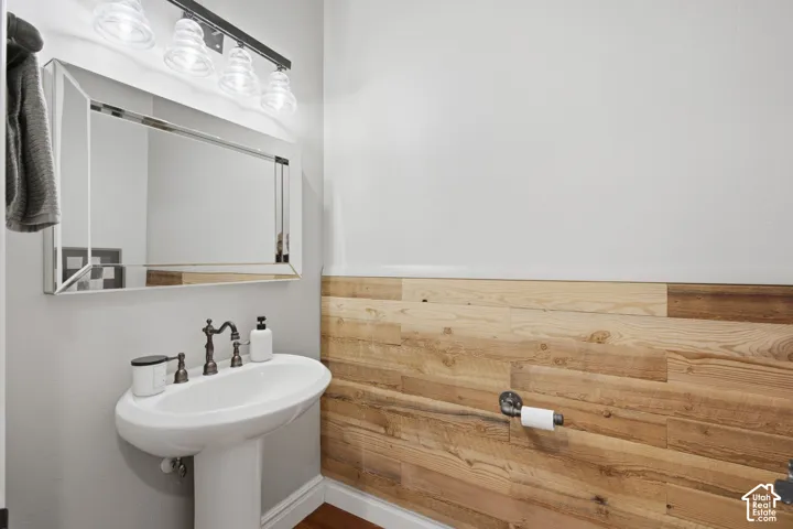 Powder room featuring horizontal wood-plank wall paneling, a white pedestal sink with oil-rubbed bronze faucet, a beveled-edge wall mirror, and a four-light vanity fixture