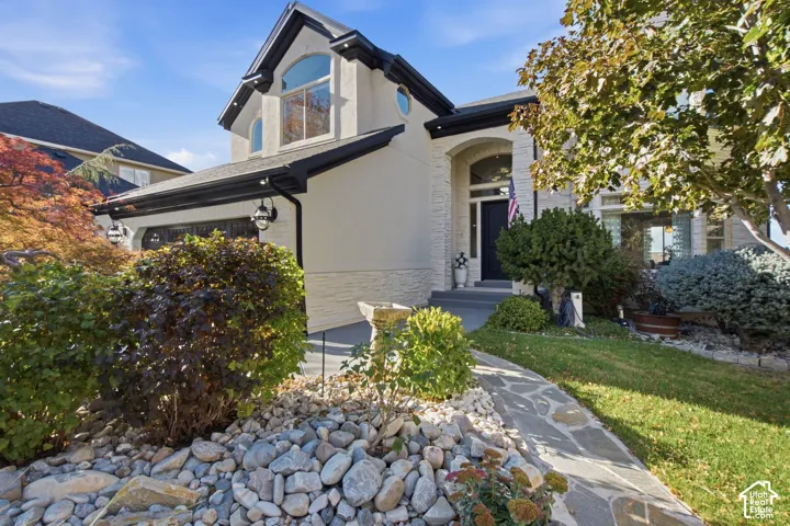 Stucco and stacked stone facade featuring a multi-gabled roofline, arched entryway, and flagstone walkway