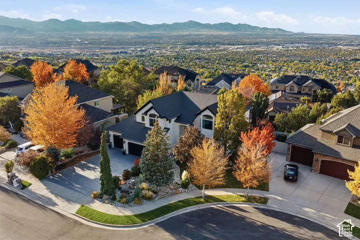 Aerial perspective of a multi-gabled residence featuring a concrete driveway, attached multi-car garage, manicured landscaping, and a mountain backdrop