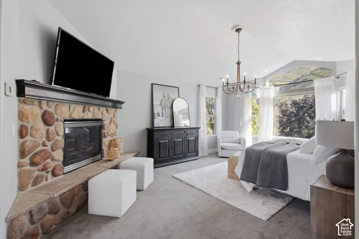 Vaulted ceilings featuring a floor-to-ceiling stone fireplace, tiered hearth, and a multi-light chandelier, complemented by large windows with mountain scenery