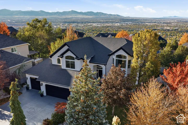 Multi-level residence featuring a light-colored brick exterior, a multi-gabled roofline with dark shingling, arched architectural windows, a multi-car garage with dark-finish doors, and panoramic mountain backdrop
