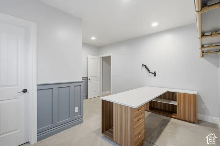 Built-in L-shaped desk featuring cabinetry with wood-finish veneer, a smooth solid-surface countertop, recessed LED lighting, and decorative wainscoting