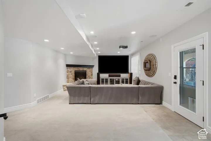 Spacious room featuring recessed ceiling lighting, a corner fireplace with stone veneer and a dark wood mantel, neutral carpeting, and a glass-paneled exterior door