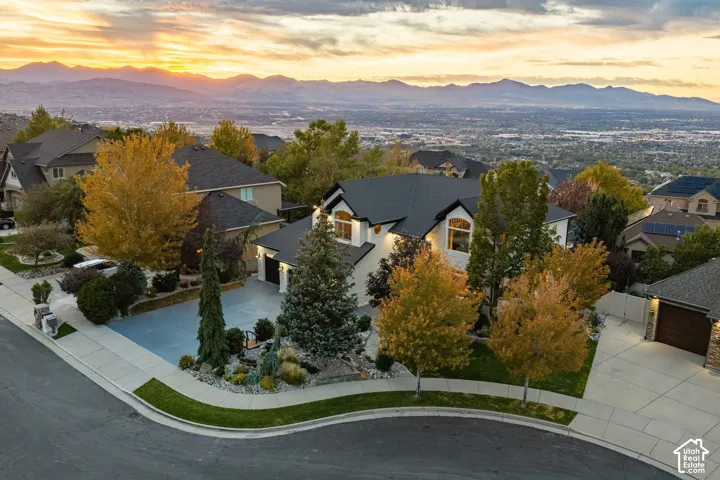 Elevated property featuring a multi-gabled roofline, concrete driveway, stone and masonry exterior, and mature landscaping, framed by expansive mountain and valley scenery