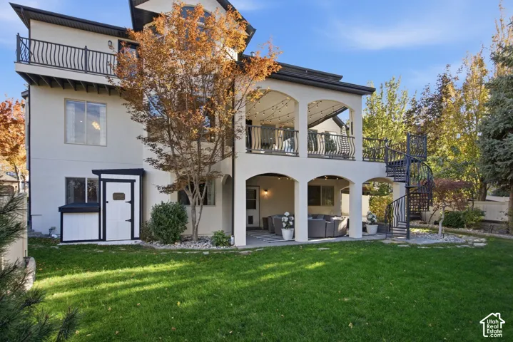 Multi-level stucco exterior featuring a covered patio, second-story deck with metal railing, black spiral staircase, and exterior storage shed