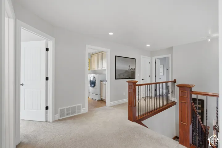 Staircase landing featuring a wood handrail with decorative metal balusters, neutral carpeting, and recessed lighting
