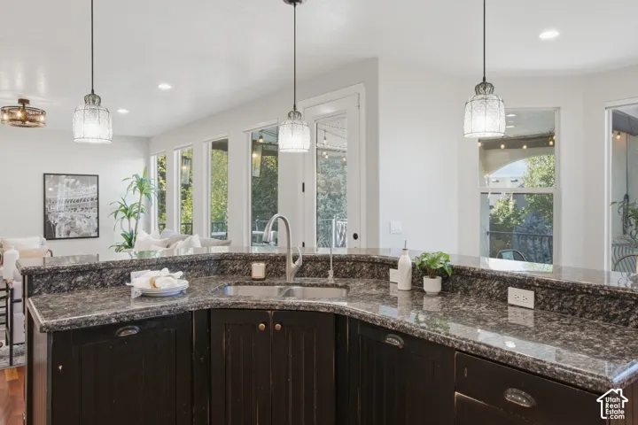 Kitchen featuring dark cabinetry, expansive stone countertops, a dual-basin undermount sink with a gooseneck faucet, and three pendant light fixtures