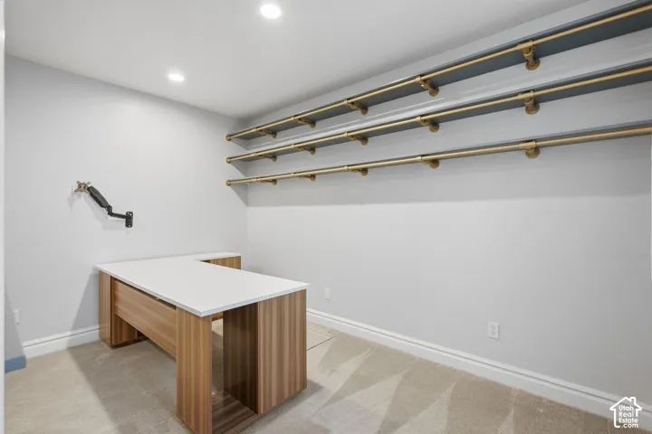 Built-in wood-finish L-shaped desk with stone-finish surface, recessed lighting, and wall-mounted brass-finish shelving units