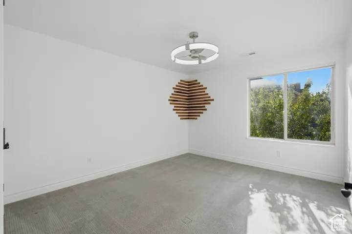 Neutral-toned carpeting, large window with natural light, geometric wood-slat wall installation, and modern LED circular ceiling fan
