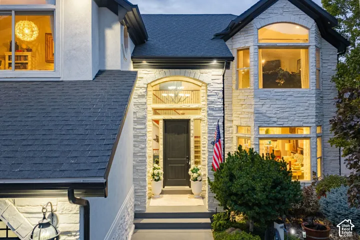 Architectural exterior featuring white stone facade, arched entryway, shingle roofing, multi-paned windows, and dark-toned trim