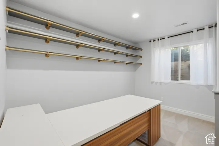 Custom built-in desk with wood-finish cabinetry and a white surface, complemented by three wall-mounted industrial-style metal garment rods and recessed lighting