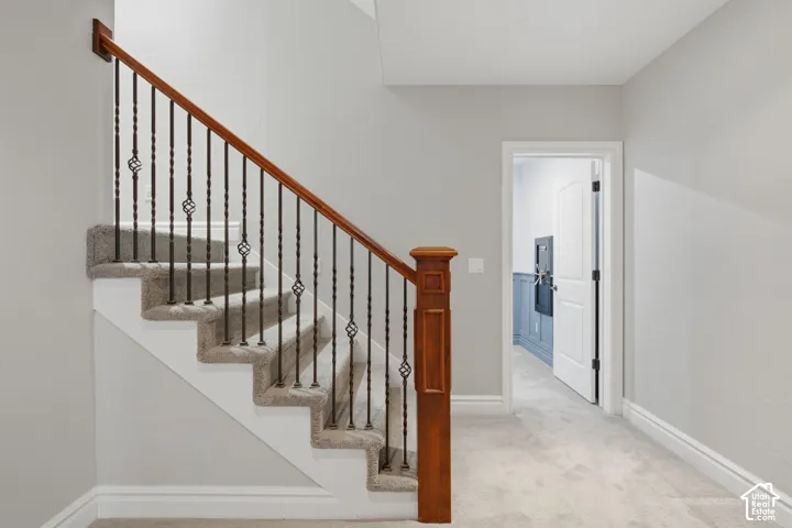 Staircase featuring a wooden handrail, decorative metal balusters, and carpeted treads