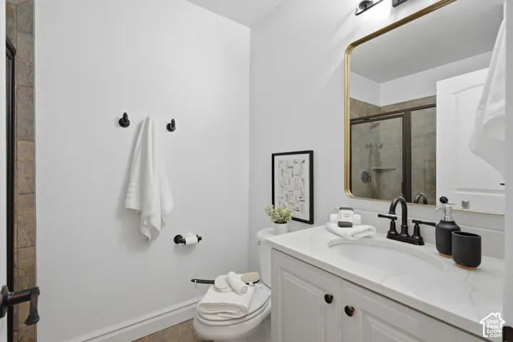 Bathroom featuring a white vanity with a light-toned countertop, undermount sink, matte black widespread faucet, rectangular wall mirror with a gold-tone frame, and a walk-in shower with tiled surround
