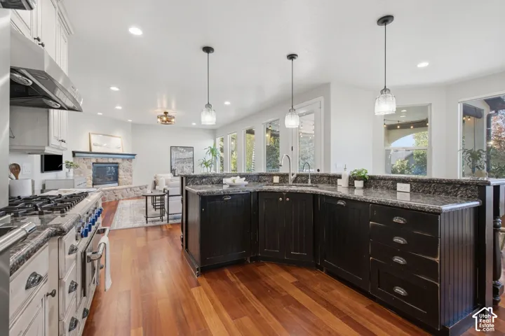 Kitchen featuring dark cabinetry, expansive stone-surface countertops, professional-grade gas range, wood-finish flooring, and pendant lighting