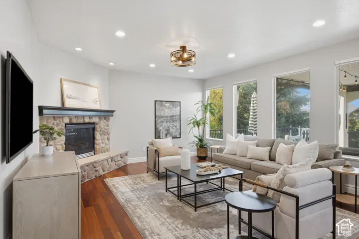 Living space featuring wood-finish flooring, a corner stone-surround fireplace with a wooden mantel, recessed lighting, and large windows