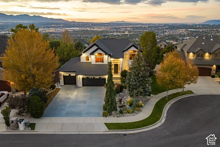 Two-car garage with dark wood-finish doors, expansive driveway, established landscaping, and a curvilinear sidewalk