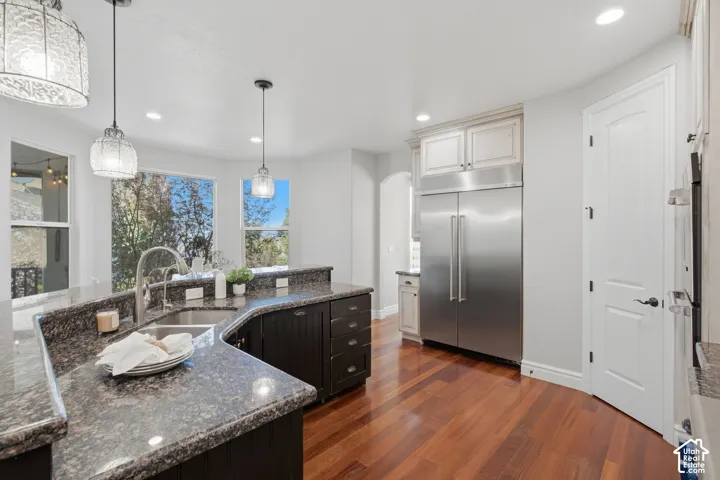 Kitchen featuring dark-toned cabinetry, stone countertops, wood-finish flooring, stainless steel side-by-side refrigerator, and multi-pendant lighting