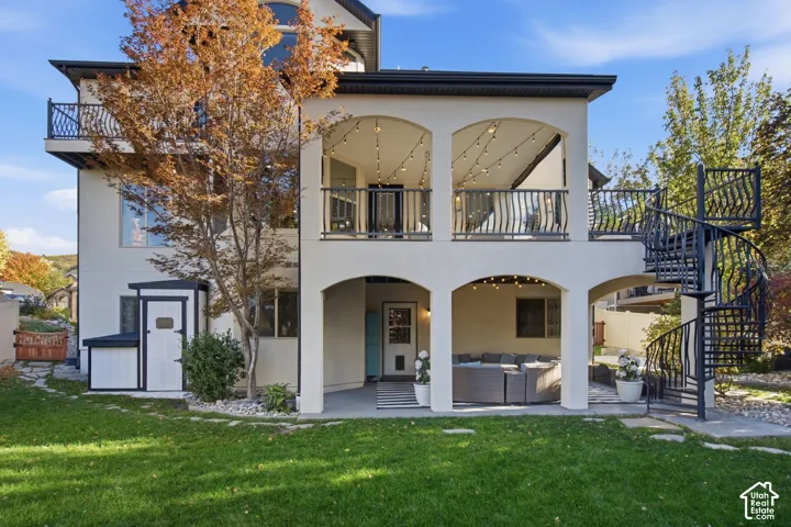 Multi-level exterior featuring a covered patio, an elevated balcony, a black metal spiral staircase, and stucco siding