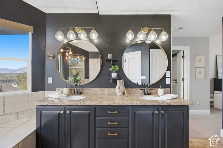 Double vanity featuring a stone countertop, dual undermount sinks, matte black fixtures, circular mirrors, and integrated multi-bulb wall lighting
