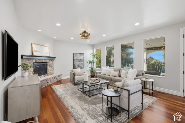 Living area featuring wood-finish flooring, a stone-surround corner fireplace with a dark mantel, recessed lighting, and multiple tall windows
