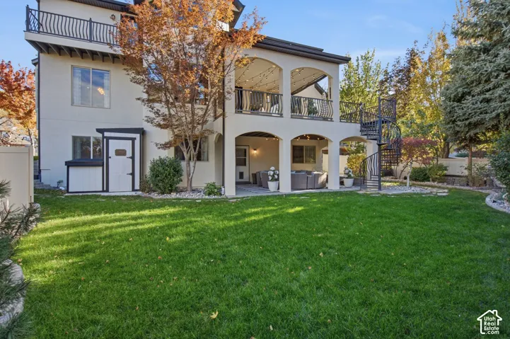 Exterior featuring a two-level covered patio, a metal spiral staircase, second-story balcony with metal railing, and a landscaped lawn