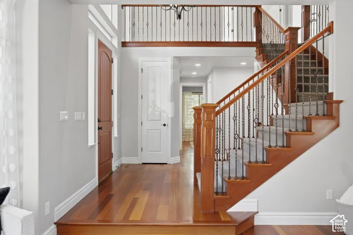 Grand entryway featuring wood-finish flooring, a wood-trimmed staircase with wrought iron balusters, a multi-paneled wood entry door, and a second-story mezzanine railing