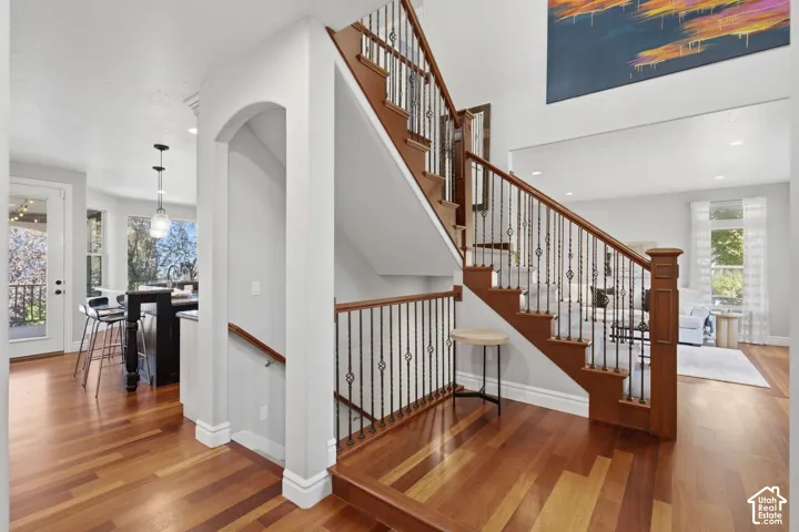 Staircase featuring wood treads, square newel posts, and decorative metal balusters, complemented by wood-finish flooring and an arched architectural opening