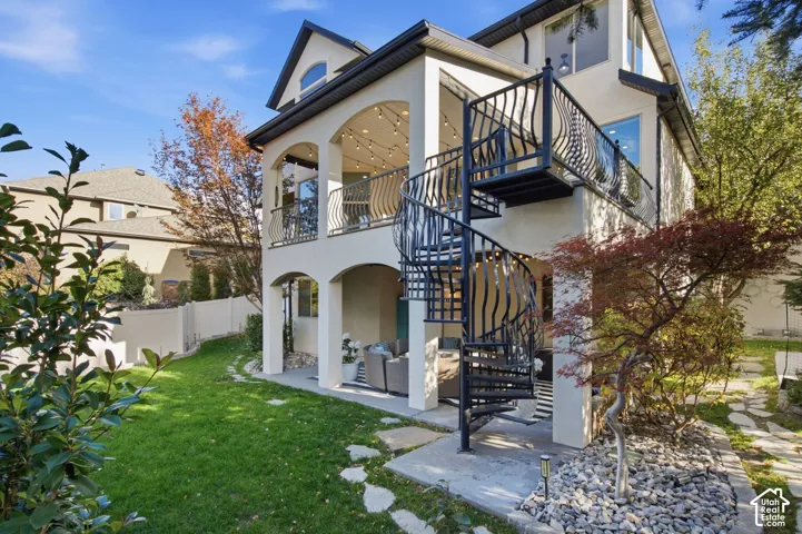 Multi-level exterior featuring a covered patio, a second-story balcony with metal railings, a spiral staircase, and stone-accented landscaping