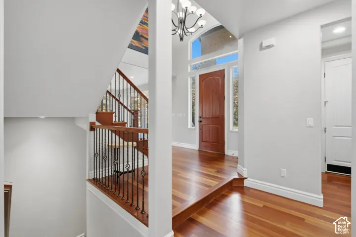 Entryway featuring wood-finish flooring, a raised wooden staircase with metal balusters, an arched solid wood front door, and a multi-light chandelier
