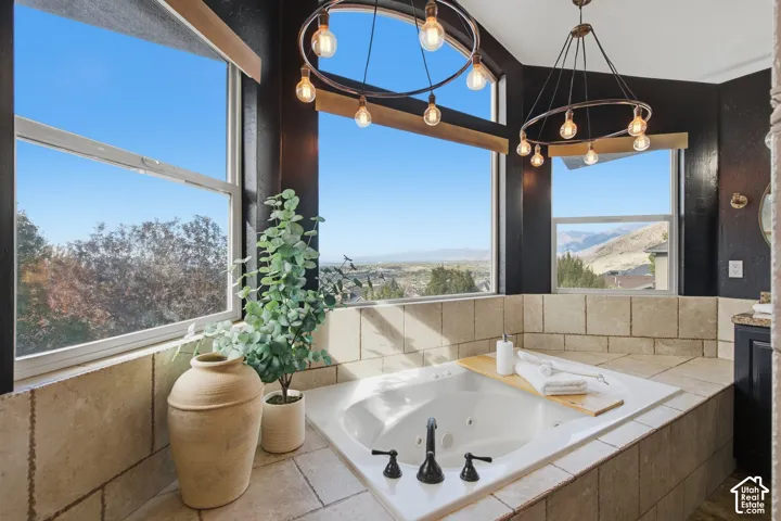Jetted soaking tub with tile surround, dual circular pendant lighting, and large windows featuring mountain and landscape scenery