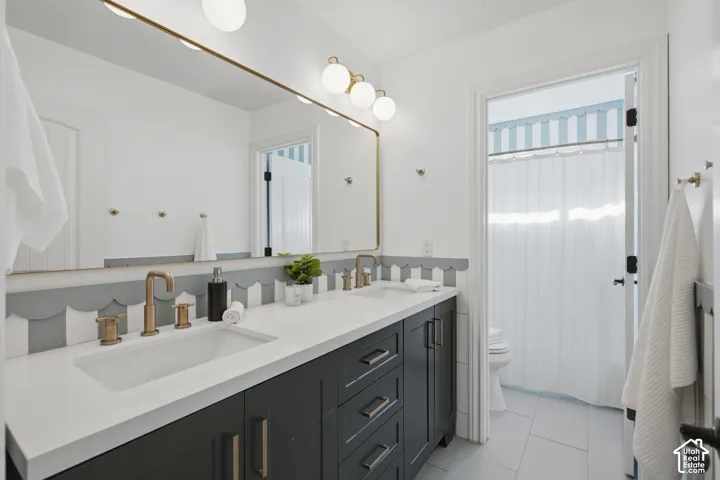Double vanity featuring dark cabinetry, solid-surface white countertops, scalloped wall detailing, metallic hardware, and gold-finish fixtures