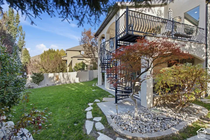 Backyard exterior featuring a raised deck with metal railings, a black spiral staircase, a covered patio, and flagstone hardscaping