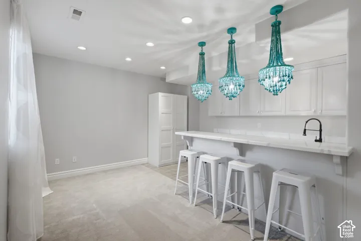 Built-in wet bar featuring stone-finish countertops, white cabinetry, a black gooseneck faucet, three tiered teal-beaded chandeliers, and recessed ceiling lighting