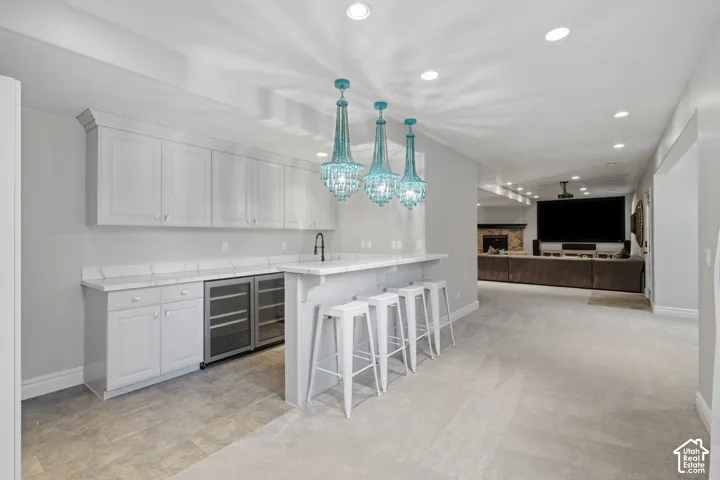 Wet bar featuring white cabinetry, stone countertops, two built-in beverage refrigerators, and three pendant light fixtures