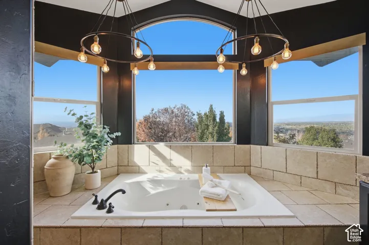 Sunken jetted tub featuring a tile surround, dual circular pendant lighting, and an arched window