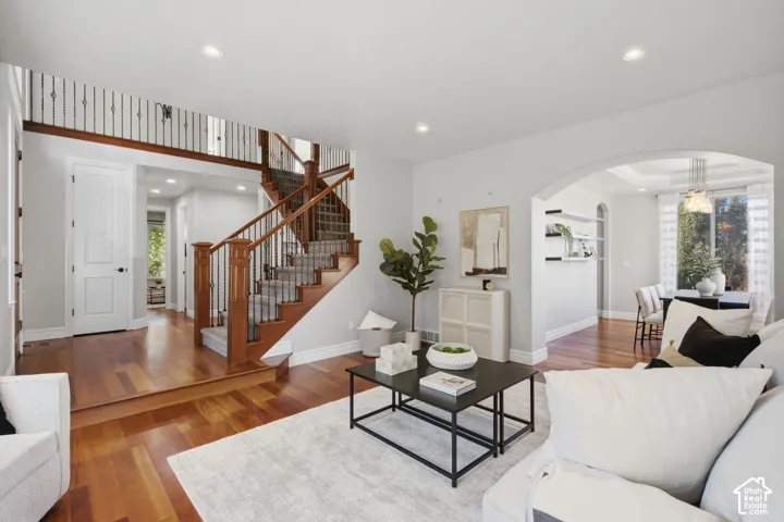 Open-concept living space featuring wood-finish flooring, recessed lighting, arched wall openings, a wooden staircase with metal balusters, and built-in floating wall shelving