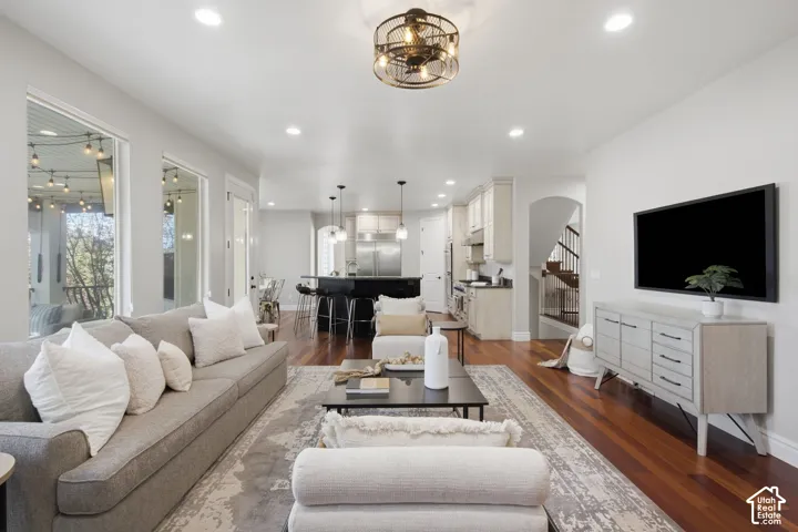 Open-concept living space featuring wood-finish flooring, recessed lighting, a cage-style ceiling fan, a kitchen island with stone countertop, and an arched entryway