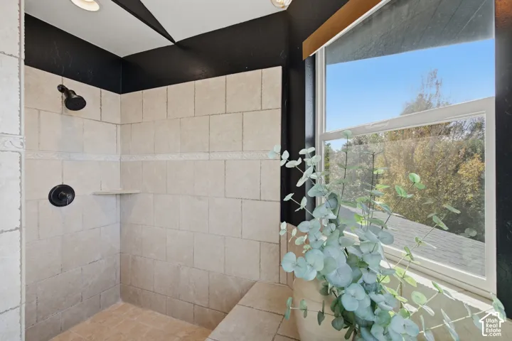 Walk-in shower featuring large-format tile surround with decorative accent banding, built-in corner shelving, integrated tile bench, and matte black plumbing fixtures