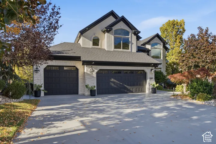 Multi-level exterior featuring stone and stucco siding, a three-car garage, arched windows, and a paved driveway