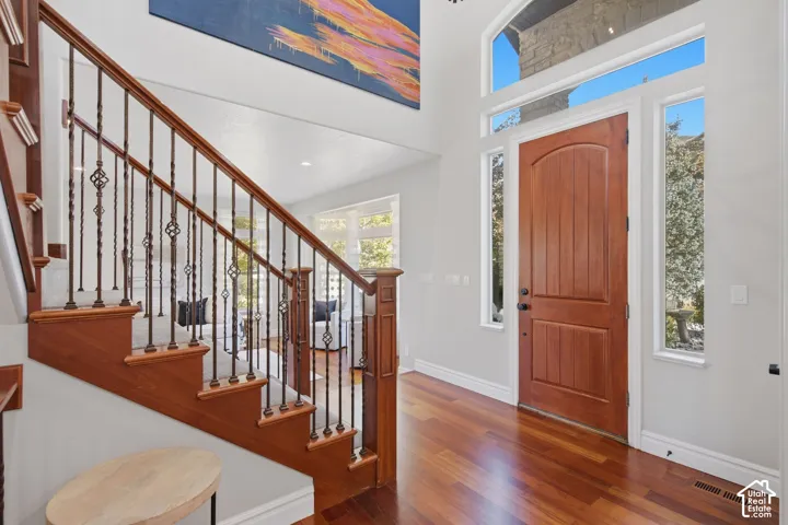 Foyer featuring double-height ceilings, natural wood-finish flooring, a solid wood entry door, arched transom window, and a staircase with stained wood handrails and decorative metal balusters