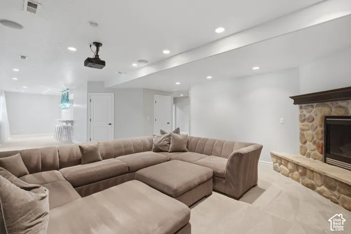Spacious room featuring a stone-faced fireplace with a wood mantel and raised hearth, recessed lighting, ceiling-mounted projector, and a built-in wet bar with pendant lighting