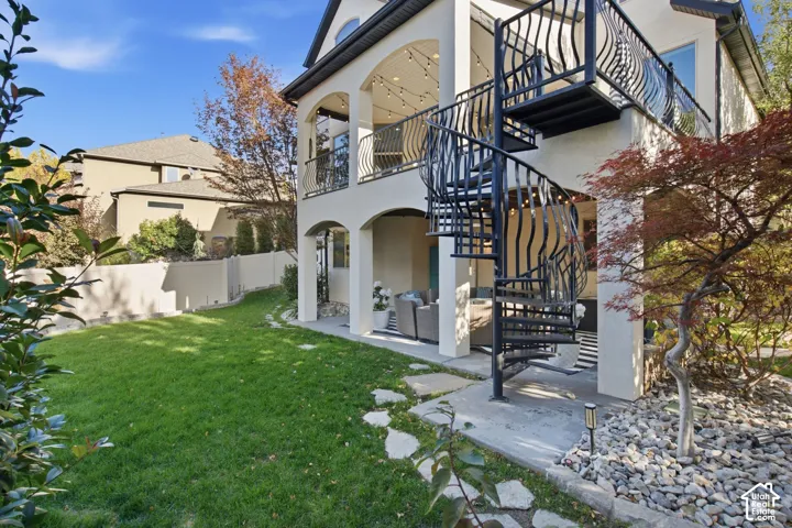 Multi-level exterior featuring a covered patio, wrought iron spiral staircase, arched architectural details, second-story balcony, and landscaped yard with stone paver accents