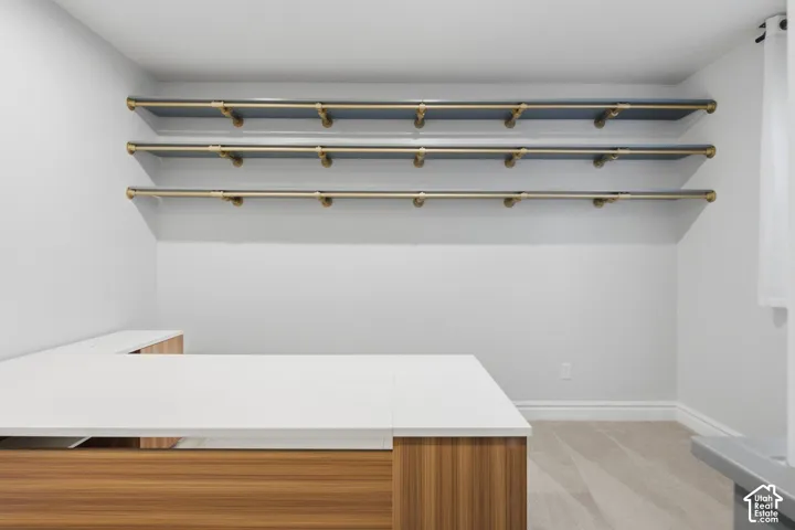 Built-in L-shaped desk with a light-toned wood-finish base and solid white countertop, complemented by three tiers of wall-mounted shelves featuring metallic support brackets and rods