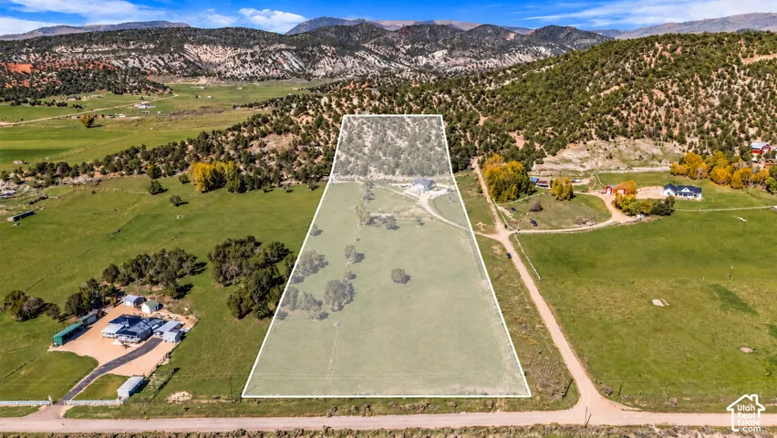 Expansive green acreage with scattered mature trees and mountainous terrain