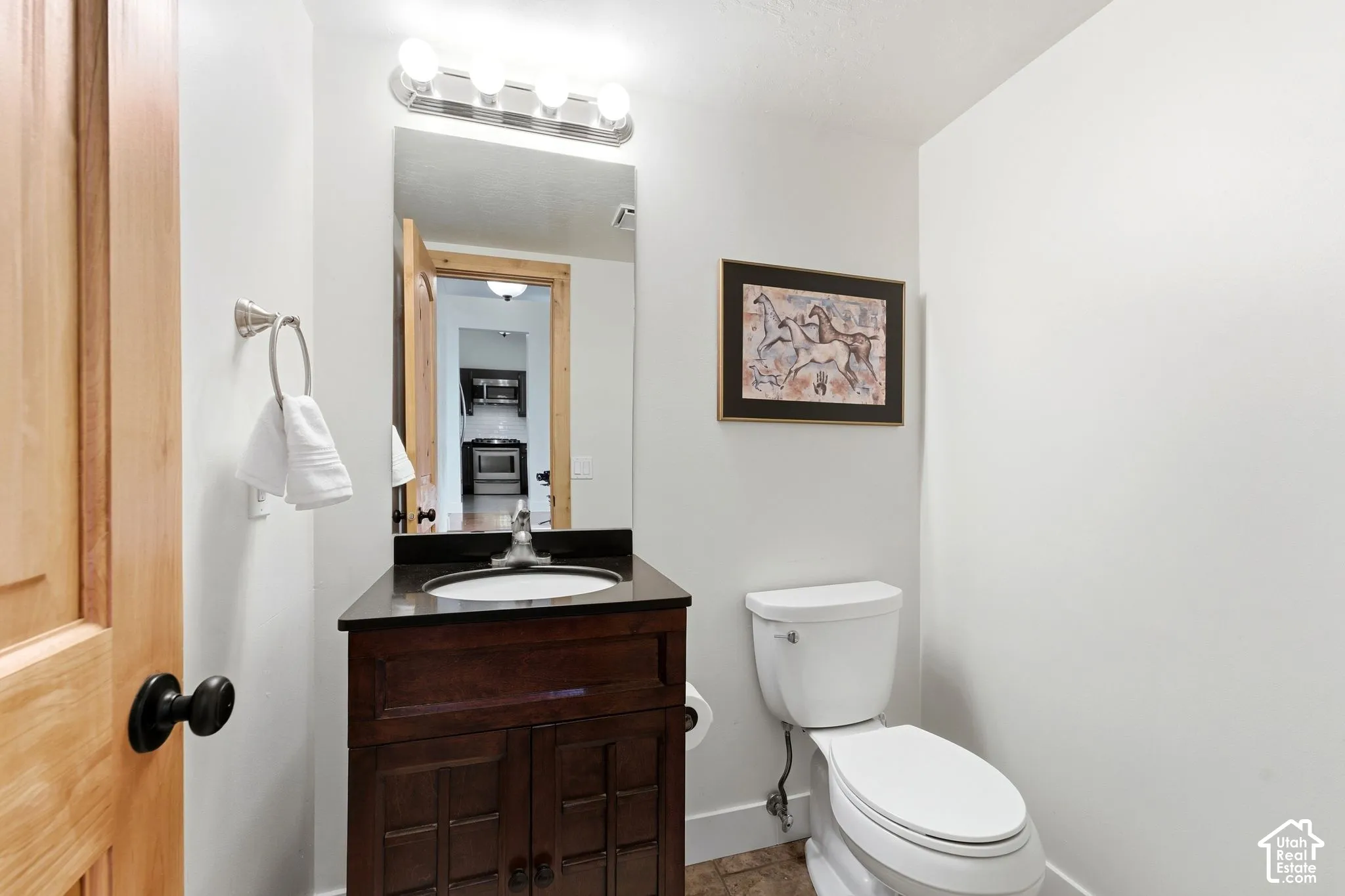 Hardwood door, vanity with dark countertop, white toilet, and tile flooring