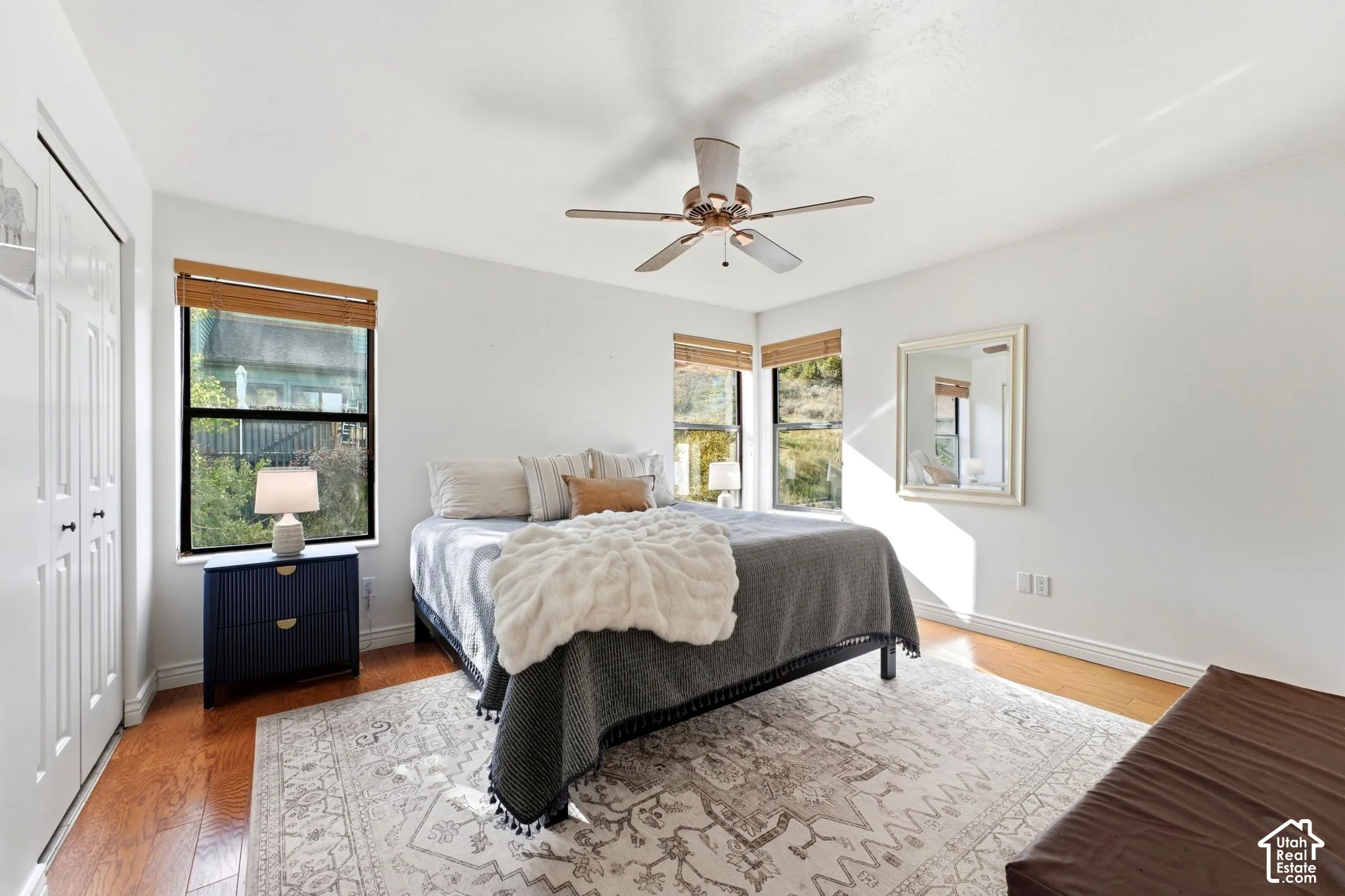 Hardwood-finish flooring with white baseboards, a ceiling fan with light fixture, and two windows with natural wood-tone blinds