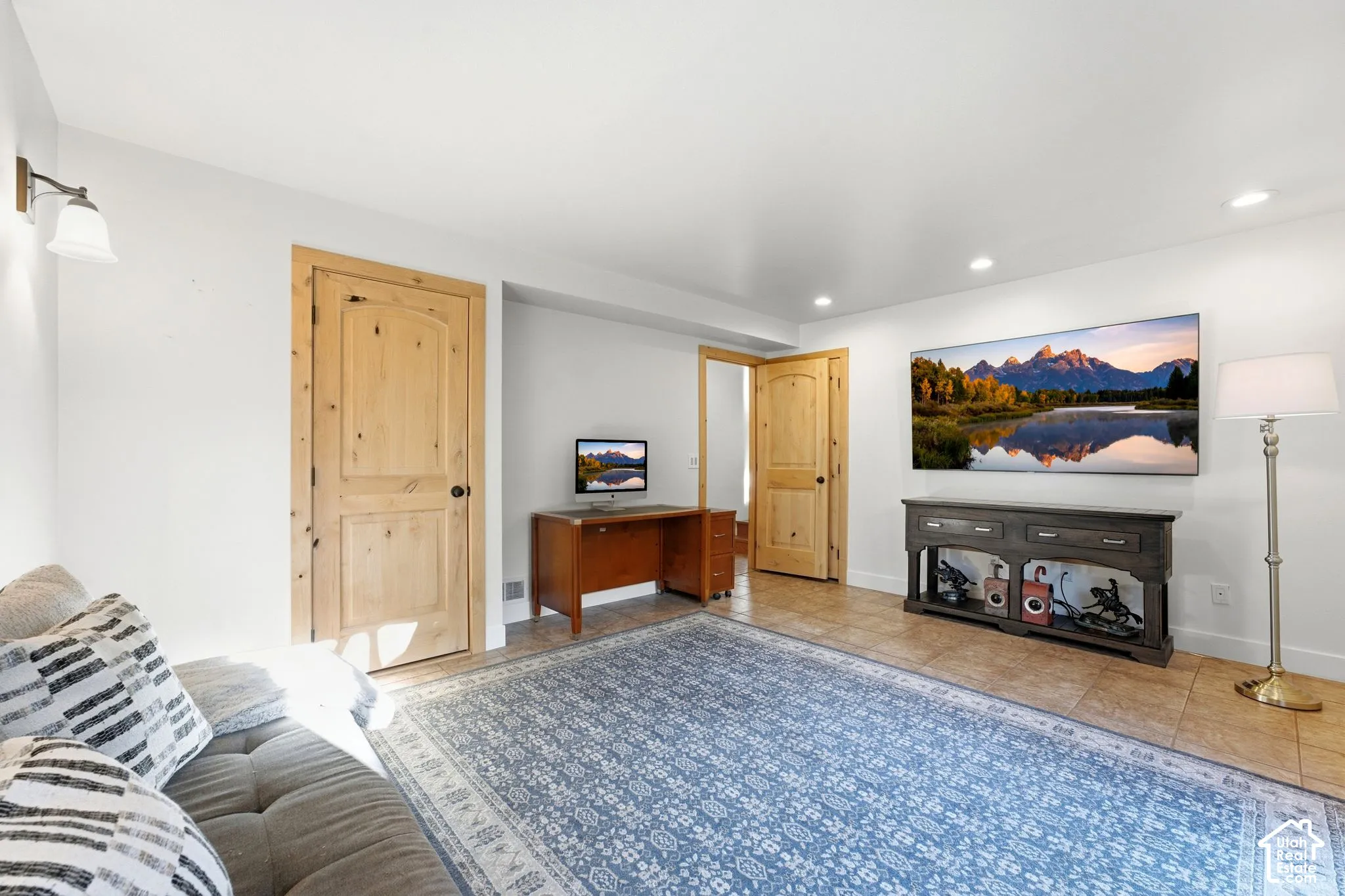 Recessed lighting and a wall sconce illuminate the space featuring wood-finish doors and tile flooring